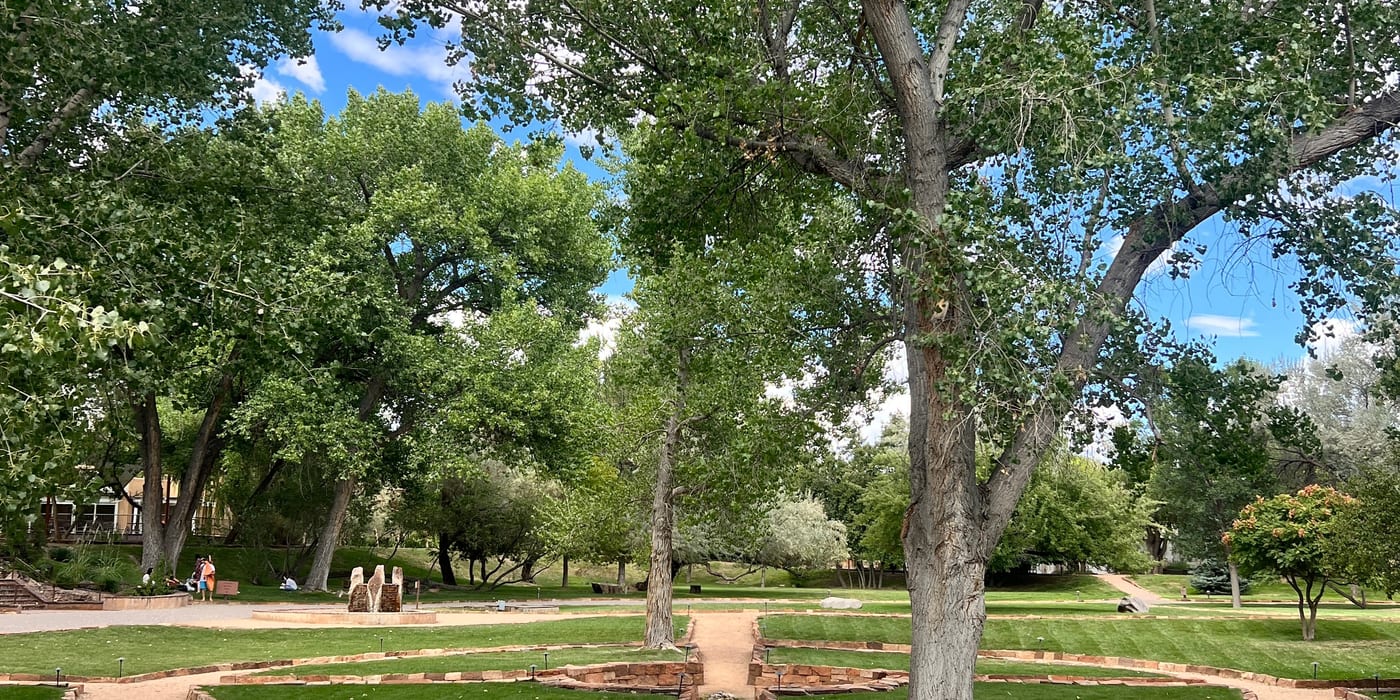 Tree-lined pathway at Ojo Santa Fe Spa Resort with red sandstone borders and lush green grounds