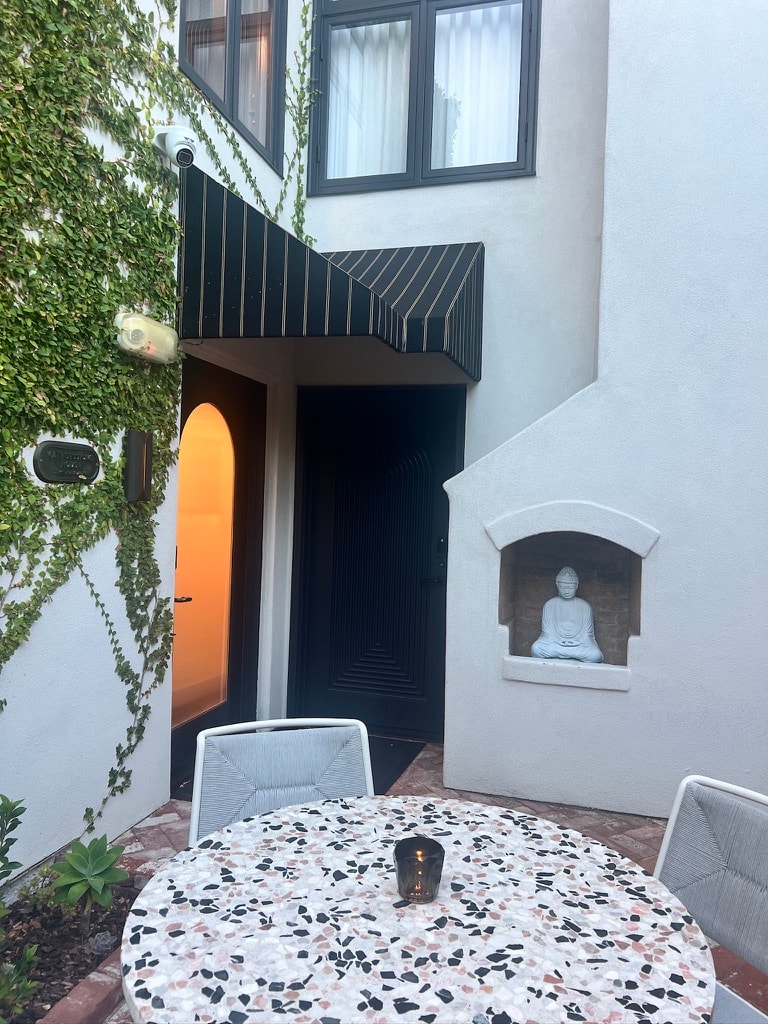 Orli La Jolla courtyard at dusk — ivy-covered white stucco walls, a terrazzo table, and a Buddha sculpture set into an arched niche