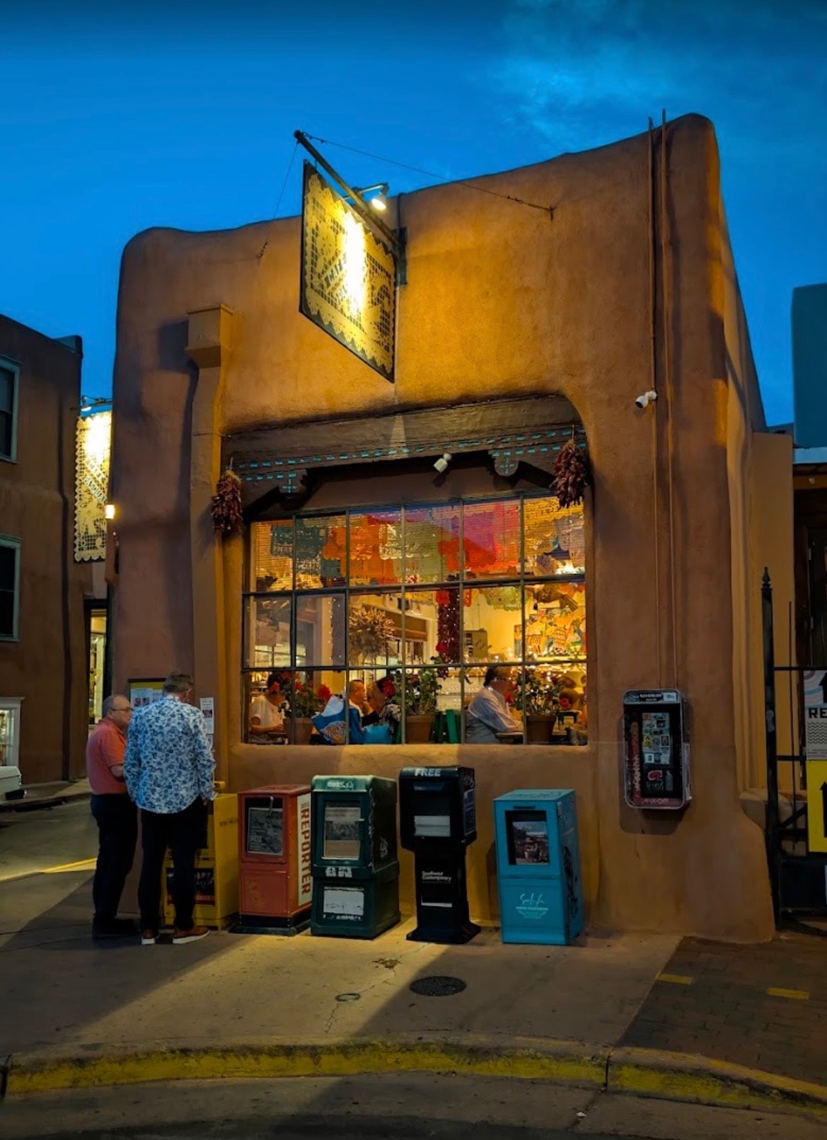 Cafe Pasqual's restaurant exterior at dusk, Santa Fe, New Mexico — the iconic hand-painted sign and illuminated adobe storefront